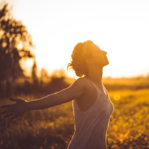 Woman breathing deeply in sunshine, representing personal growth and presence